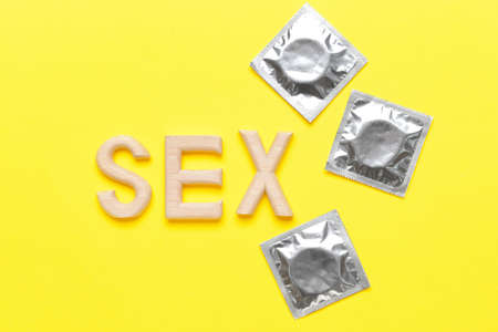 Word SEX with condoms on color background