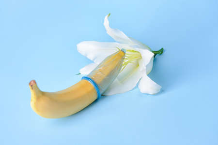 Banana in condom and flower on color background. Erotic conceptの写真素材