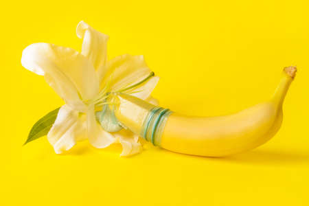 Banana in condom and flower on color background. Erotic conceptの写真素材