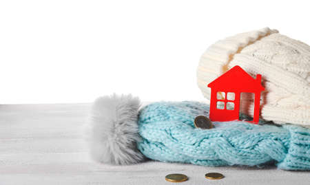 Figure of house, coins and warm hats on table against white background. Concept of heating seasonの写真素材