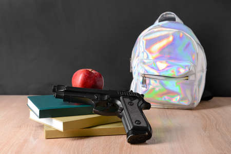 Pistol with books and backpack on table in classroom. Concept of school shooting