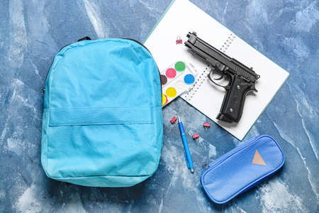 Pistol and backpack with stationery on color background. Concept of school shooting