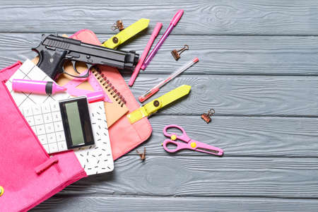 Pistol and backpack with stationery on wooden background. Concept of school shooting