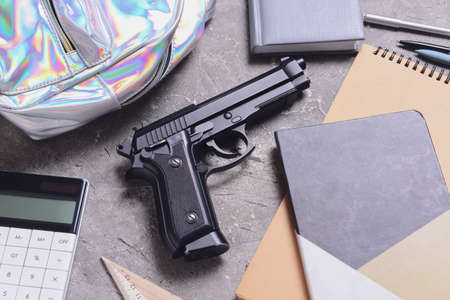 Pistol and backpack with stationery on grunge background. Concept of school shootingの写真素材