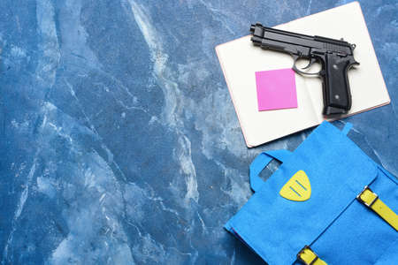 Pistol and backpack with notebook on color background. Concept of school shooting