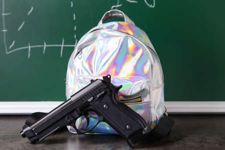 Pistol and backpack on table in classroom. Concept of school shooting
