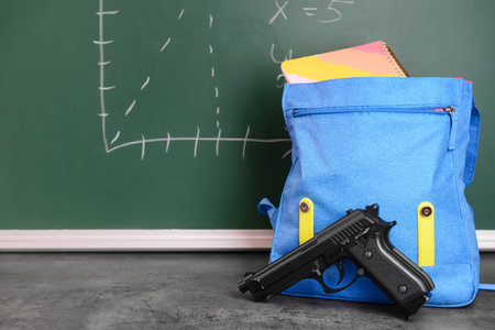 Pistol and backpack on table in classroom. Concept of school shootingの写真素材