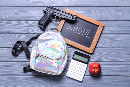 Pistol and backpack with chalkboard on wooden background. Concept of school shootingの写真素材