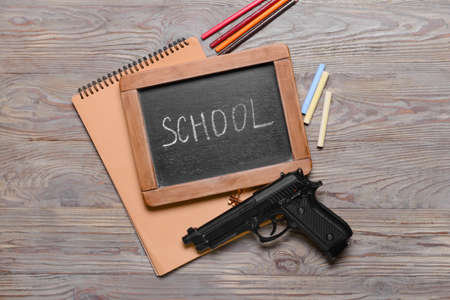 Pistol and chalkboard with stationery on wooden background. Concept of school shootingの写真素材