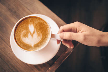 Woman with cup of latte at table in cafeの写真素材