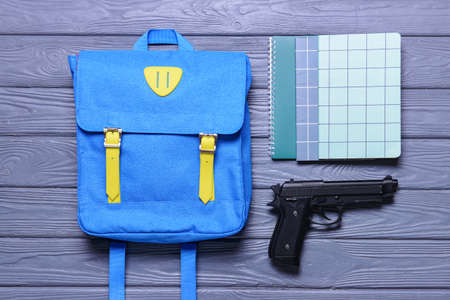Pistol and backpack with notebooks on wooden background. Concept of school shootingの写真素材