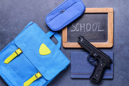 Pistol and backpack with chalkboard on dark background. Concept of school shooting