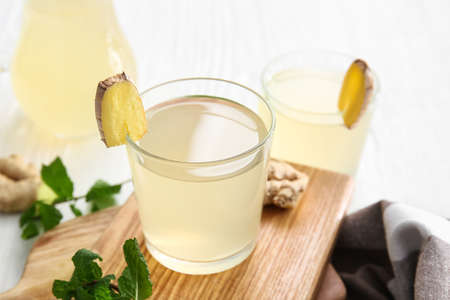 Board with glass of healthy ginger juice on light backgroundの写真素材