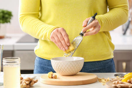 Woman grating ginger at table in kitchenの写真素材