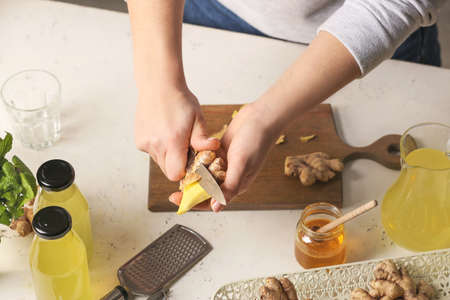 Woman peeling ginger with knife at table in kitchen