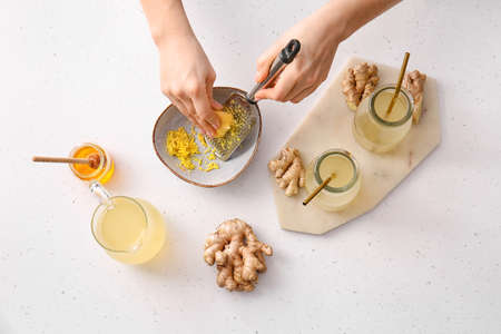 Woman grating ginger on light background