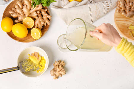 Woman pouring healthy ginger juice from jug into glass on light backgroundの写真素材