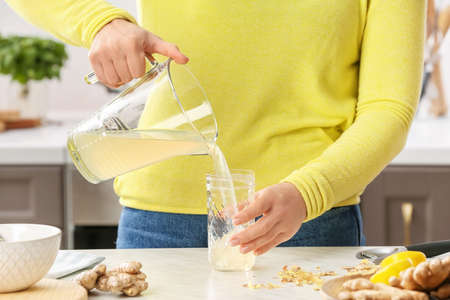 Woman pouring healthy ginger juice from jug into jar at table in kitchenの写真素材
