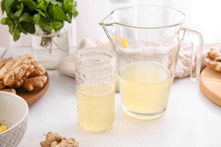 Jug and glass of healthy ginger juice on table