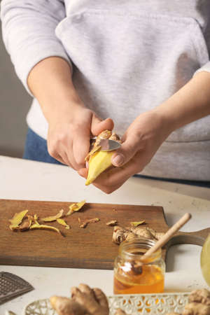 Woman peeling ginger with knife at table in kitchenの写真素材