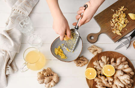 Woman grating ginger on white wooden background