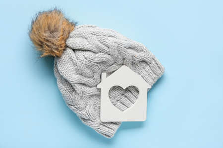 Figure of house and warm hat on color background. Concept of heating seasonの写真素材