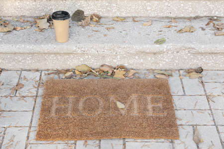 Doormat with cup of coffee near entrance of house on autumn dayの写真素材