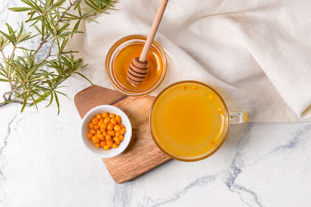 Cup of healthy sea buckthorn tea with honey on table
