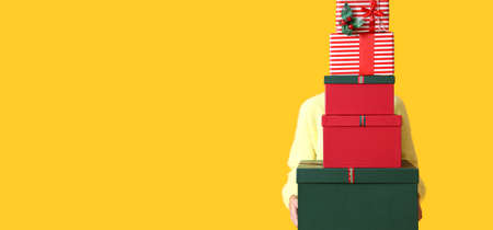 Young woman holding many Christmas gifts on color background with space for text