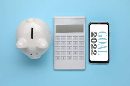 Calculator with mobile phone and piggy bank on color background. New Year 2022 goals