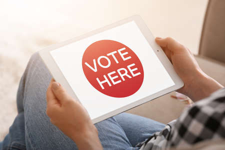 Young woman holding tablet computer with text VOTED HERE on screen