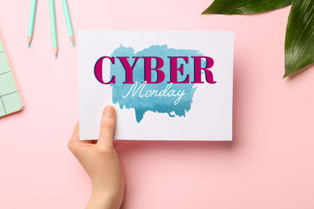 Female hand holding sheet of paper with text CYBER MONDAY on pink background
