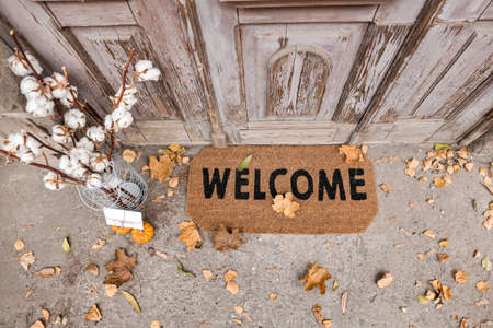 Doormat with cotton flowers and letter near entrance of house on autumn dayの写真素材