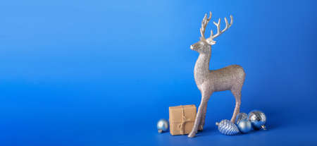 Reindeer with Christmas decor and gift on blue background with space for textの写真素材