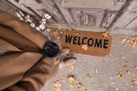 Woman with cup of coffee standing near doormat outdoorsの写真素材
