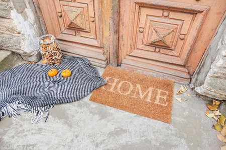 Doormat with plaid, pumpkins and leaves near entrance of house on autumn dayの写真素材