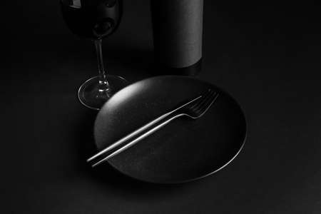 Stylish table setting with glass and bottle of wine on dark backgroundの写真素材