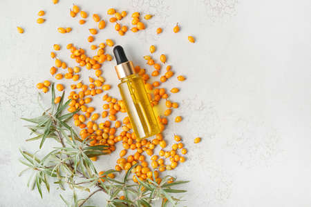 Bottle of sea buckthorn essential oil on light background