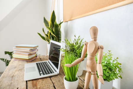 Books, laptop, wooden mannequin and houseplants on table in roomの写真素材