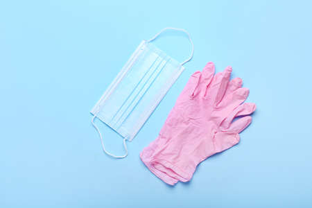 Medical mask and protective gloves on color background