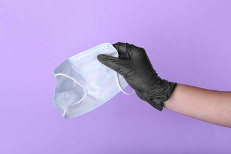 Female hand in protective glove with medical mask on color background
