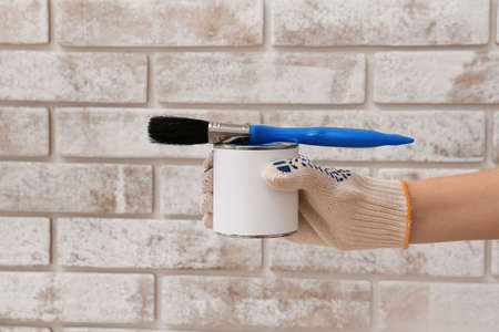 Female hand with can of paint and brush on brick backgroundの写真素材