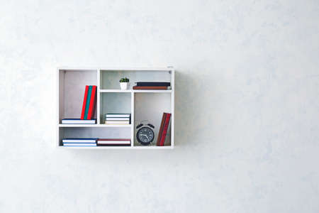 Shelf with books and alarm clock hanging on light wallの写真素材