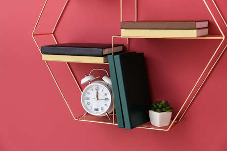 Shelf with books and alarm clock hanging on color wall, closeupの写真素材