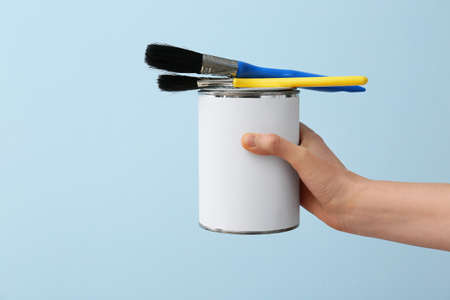 Female hand with can of paint and brushes on color backgroundの写真素材