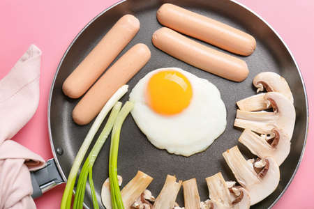 Frying pan with tasty egg, sausages, mushrooms and onion on color backgroundの写真素材