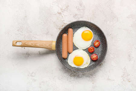Frying pan with tasty eggs, sausages and tomatoes on light backgroundの写真素材