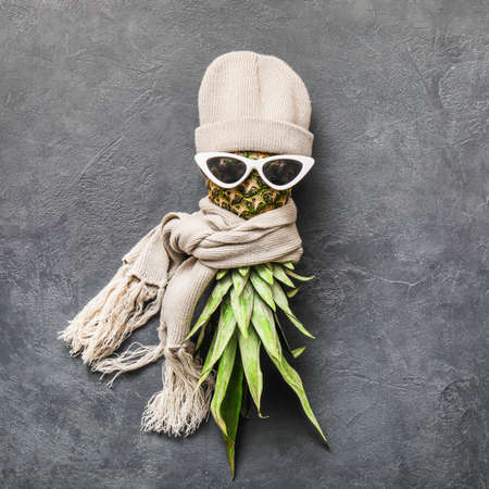 Creative composition with pineapple, sunglasses, warm hat and scarf on dark backgroundの写真素材