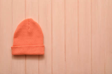 Stylish warm hat on color wooden background