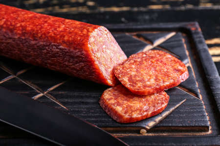Cutting board with tasty salami on dark wooden backgroundの写真素材